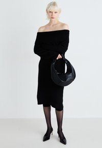 Abito nero a spalle scoperte, di lunghezza media, indossato con collant neri trasparenti e tacchi a punta. Borsa hobo in pelle nera tenuta in mano.