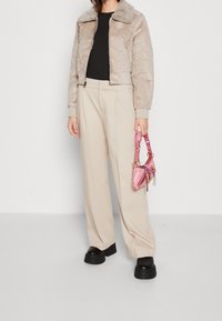 Lekka beżowa kurtka z krótkim futerkiem z kołnierzem, w połączeniu z beżowymi spodniami z wysokim stanem i małą różową torebką. Czarne masywne buty na platformie.