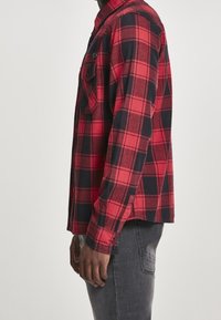 Röd och svart rutig flanellskjorta med krage, långa ärmar och bröstficka, med knappar på ärmsluten och detalj i sidsömmen.