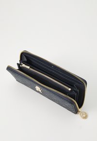 Portafoglio in pelle navy con chiusura a zip, hardware dorato e motivo in rilievo. Dotato di più scomparti per carte e di un compartimento per le monete.