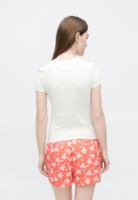 Bílé tričko s krátkými rukávy v kombinaci s červenými kraťasy s květinovým vzorem. Látka vypadá hladce, tričko má volný střih a jednoduchý kulatý výstřih.