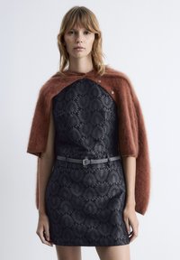 Schwarzes Kleid mit strukturiertem Blumenmuster, gewickelter Taille; geschichtet mit einem langen, rostfarbenen Mohair-Cape. Glattes Gewebe und weiche Textur.