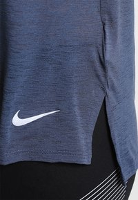 Námořnické sportovní tričko vyrobené z texturované tkaniny, s bočním rozparkem a bílým logem Nike blízko lemu.