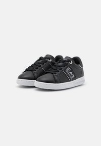 Black leather sneakers with white rubber soles, featuring a triangular logo accent and classic lace-up design. Smooth texture and rounded toe.