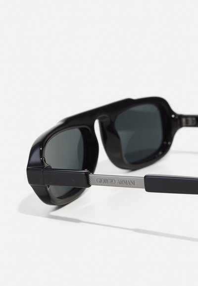 Schwarze Sonnenbrille mit grün getönten Gläsern, die ein eckiges Design aufweist. Der Bügel zeigt "Giorgio Armani" in silbernem Metall.