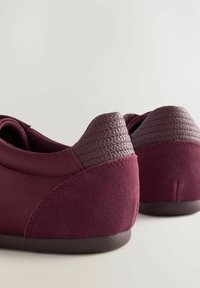 Burgundské tenisky s hladkým textilním svrškem a texturovanými tmavými koženými akcenty na patě. Zaoblený design s plochou gumovou podrážkou.