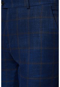 Niebieskie spodnie w kratę z teksturowanej tkaniny o subtelnej połyskliwości, podkreślone ciemnobrązowymi liniami tworzącymi wzór w kratę.