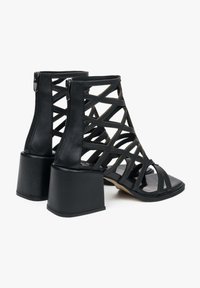 Zwarte open teen hoge hakken sandalen met een kruisbandontwerp, gemaakt van leer, met een chunky hak en een rits aan de achterkant.