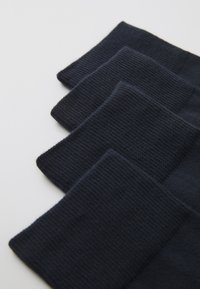 Calze a maglia di un blu navy scuro esposte in fila, caratterizzate da una trama a coste e un design a polsino rettangolare, con una superficie superiore liscia.