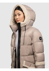 Geacă puf beige deschis cu căptușeală plușată de culoare crem. Are glugă, închidere cu fermoar frontal și buzunar lateral cu margine de blană.