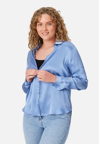 Light blue satin button-up shirt with a soft texture, long sleeves, and a relaxed fit, styled over a black top.