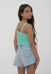 Top a fascia all'uncinetto verde menta con bordi ondulati, abbinato a pantaloni corti in denim chiaro a vita alta con orli sfrangiati e tasche posteriori.