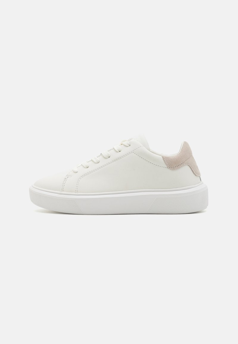 White leather sneaker with a textured beige heel accent, flat laces, and a thick white rubber sole. Minimalistic design.