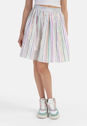 Kvinde iført et hvidt skørt med lodrette flerfarvede striber, sølvfarvet taljebånd, hvid cropped top og pastelfarvede grønne og pink høje sneakers.