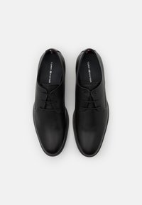 Chaussures en cuir noir avec une texture lisse, dotées d'un bout rond, de lacets et d'un logo de marque sur la semelle intérieure.