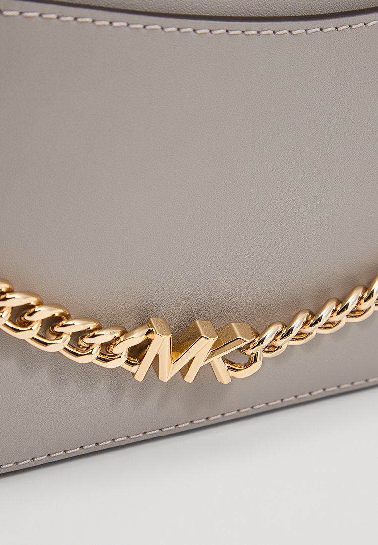 Lichtgrijze faux leren tas met een gouden kettinghandvat en een prominent gouden "MK" logo. Gladde textuur met contrasterende stikdetails.