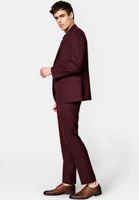 Burgundowy garnitur o dopasowanym kroju, marynarka na jeden guzik oraz spodnie typu flat-front. Połączony z brązowymi butami na podwójne zapięcia. Gładka tekstura.