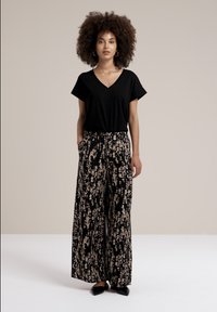Haut noir à col en V associé à un pantalon à jambes larges à motif dans des tons noir et beige ; texture lisse et coupe ample dans l'ensemble.