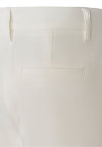 Gros plan de l'arrière d'un pantalon blanc montrant une poche passepoilée simple et des passants de ceinture sur une surface en tissu lisse.