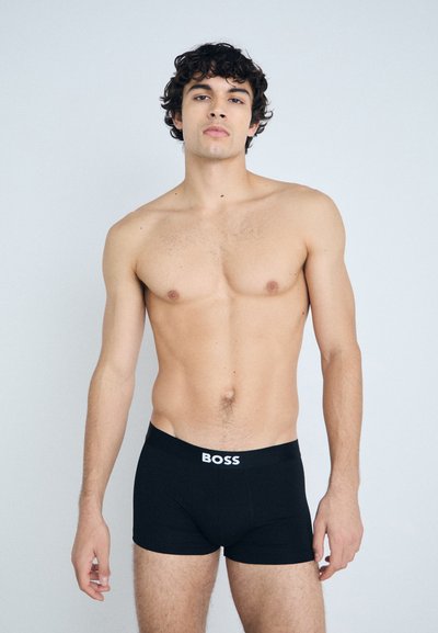 Boxers noirs avec un logo "BOSS" blanc sur la ceinture, fabriqués en tissu doux. La coupe est ajustée et le design est simple et moderne.