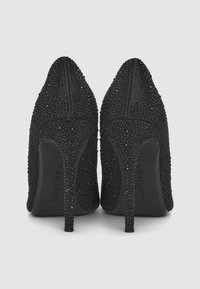 Chaussures à talons hauts noires avec une surface texturée ornée de petites perles brillantes et une pointe en amande. Les talons aiguilles offrent une élévation.