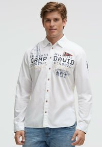 Weißes Langarmhemd mit blauen und braunen Grafiken, darunter der Schriftzug "CAMP DAVID" und ein Segelboot-Design, Knopfverschluss und kontrastierende Naht.