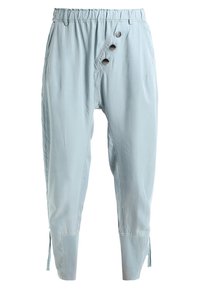 Světle modré kalhoty s volným střihem, elastickým pasem, detaily se třemi knoflíky na boku a zúženými manžetami se šňůrkami na lemu.