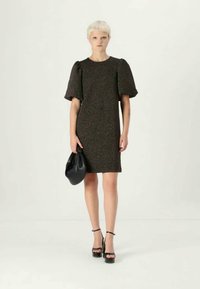 Vestido preto texturizado com mangas bufantes curtas, corte reto, combinado com uma clutch preta e sandálias de salto alto.