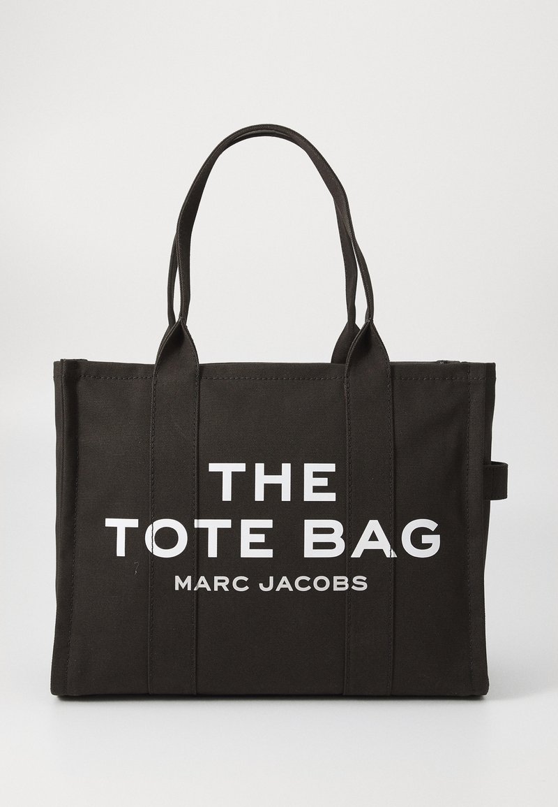 Čierna plátenná taška s dvojitými uchami. Obsahuje veľký biely nápis "THE TOTE BAG" a "MARC JACOBS." Obdĺžnikový tvar, minimalistický dizajn.