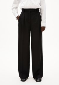 Zwarte wijde broek van gladde stof, met voorplooien en zijzakken. De taille heeft een knoopsluiting en riemlussen.