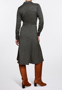 Abito a maniche lunghe di colore nero con motivo geometrico verde, con vita aderente e gonna svasata, abbinato a stivali marroni fino al ginocchio.