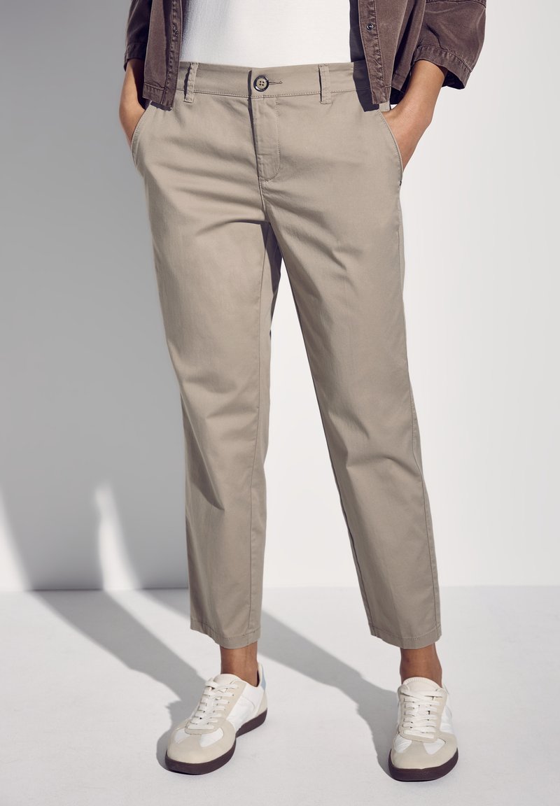 Beige cropped byxor i bomull med rak passform, som har knappstängning och sidfickor, i kombination med vita sneakers.