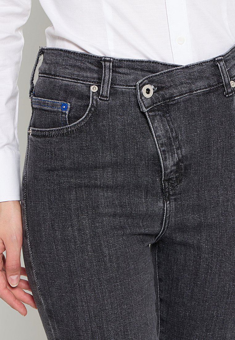 Jean en denim gris foncé au design ajusté, style à cinq poches, quincaillerie en argent et couture contrastante. Présente un accent bleu sur la poche avant.