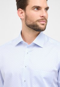 Camicia button-up azzurro chiaro con un sottile motivo a pois, dotata di colletto classico e taschino singolo sul petto. Tessuto dalla texture liscia.