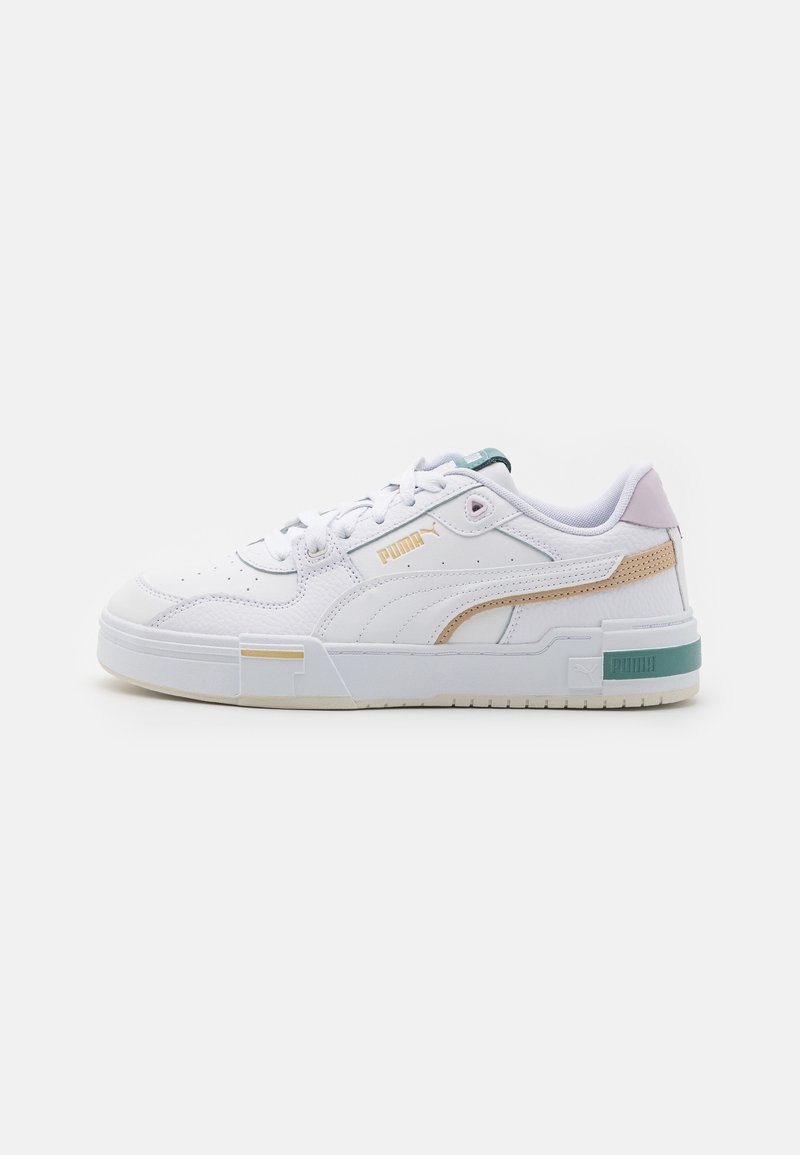 Baskets basses blanches Puma avec des accents beige et vert, bout perforé, col rembourré et détails de marque sur le côté et la semelle.