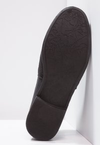 Suela de zapato negra con un patrón texturizado que presenta diseños de flores y hojas, fabricada con un material de goma duradero, mostrando un ligero desgaste en los bordes.