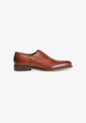 Chaussure oxford en cuir marron avec un bout arrondi, des détails cousus et un petit talon en bois. Fermeture à lacets avec cinq œillets.