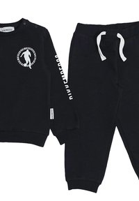 Felpa nera con logo circolare e testo bianco sulla manica, abbinata a pantaloni della tuta neri con vita regolabile.