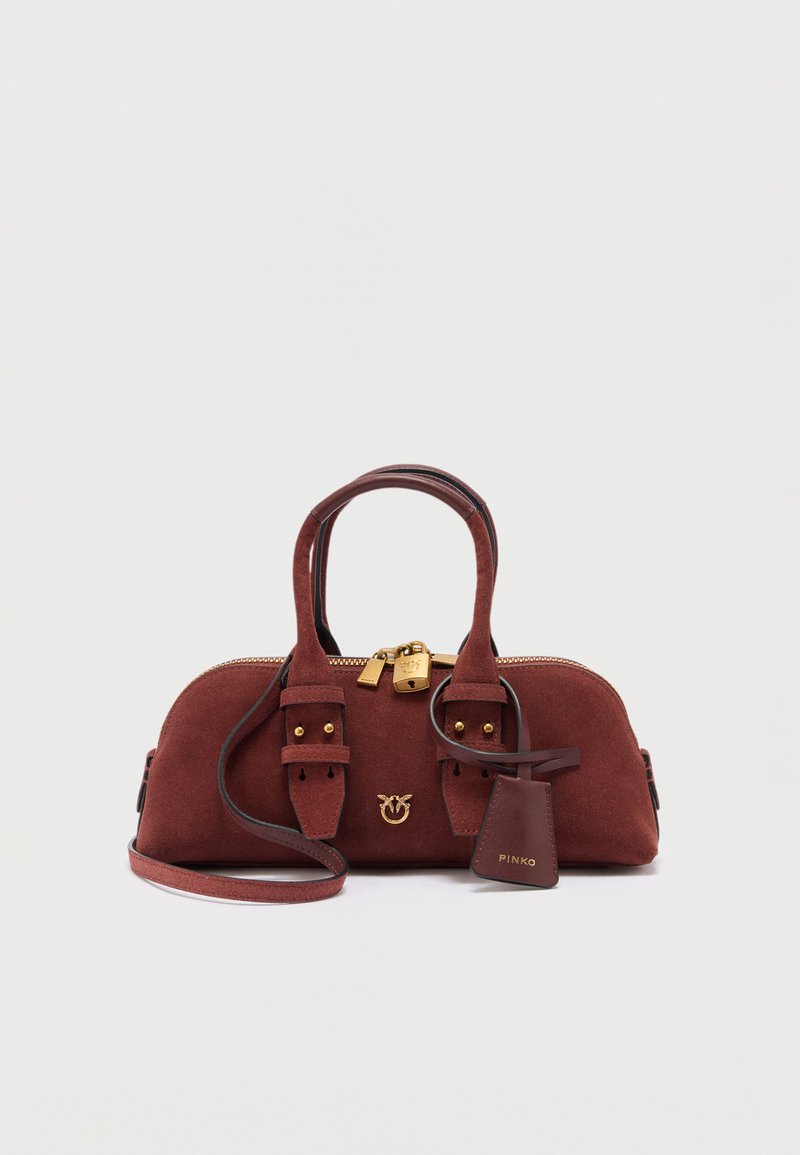 Καφέ τσάντα χειρός από σουέτ με διπλές λαβές, χρυσά μεταλλικά στοιχεία συμπεριλαμβανομένου λουκέτου και αποσπώμενο ιμάντα ώμου σε λευκό φόντο.