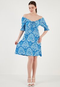 Rochie albastră cu model, cu umeri descoperiți, mâneci bufante, talie strânsă și fustă evazată. Prezintă un design detaliat cu motive florale și paisley.