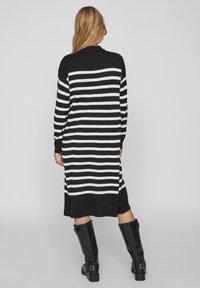 Svart och vit randig lång tröjdress med långa ärmar, ribbade manschetter och rak stil, tillsammans med knähöga svarta stövlar.