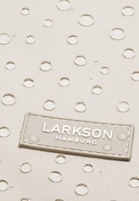Beige szövet texturált felülettel, kör alakú vízcseppekkel. Az alján egy téglalap alakú címke látható, amelyen a "LARKSON HAMBURG" felirat olvasható.
