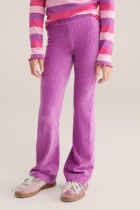 Violetit samettiset leveälahkeiset housut, joissa on pystyribbaus. Yhdistetty vaaleanpunaraidalliseen neulepuseroon ja vaaleanpunaisiin lenkkareihin, joissa on valkoiset nauhat.