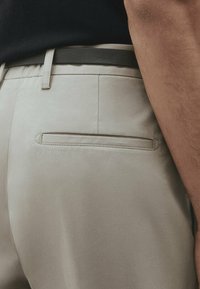 Beiga byxor har en elegant design med en bakficka, slät textur och ett mörkgrått bälte som accentuerar midjan.