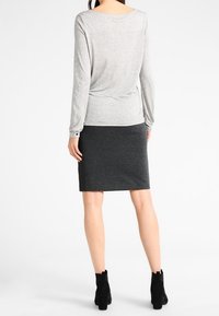 Silver long-sleeve top with a relaxed fit, paired with a fitted dark gray knee-length skirt. Black ankle boots complete the look.
