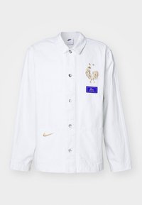 Bílá bunda s výšivkou zlatého kohouta a modrou nášivkou, se stříbrnými knoflíky a zlatým logem Nike. Součástí jsou dvě přední kapsy.