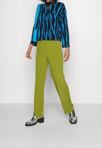 Pull noir avec des rayures bleues, pantalon large vert et mocassins argentés brillants. Un sac à main bleu et un collier en chaîne argentée sont inclus.