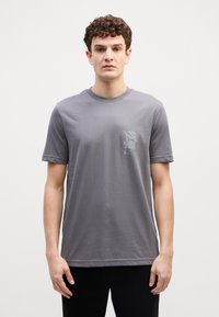 Grijze katoenen t-shirt met een ronde hals en korte mouwen. Bevat een subtiele print op het linkerborstgebied. Soepele textuur, ontspannen pasvorm.