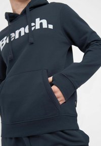 Sweat à capuche en polaire marine avec poche avant, cordon de serrage et logo blanc. Présente des poignets et un ourlet côtelés pour plus de texture et de confort.