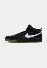 Svarte mid-top joggesko med hvit swoosh-logo, svarte snørebånd og såle av gummi, vist på en enkel lys grå bakgrunn.
